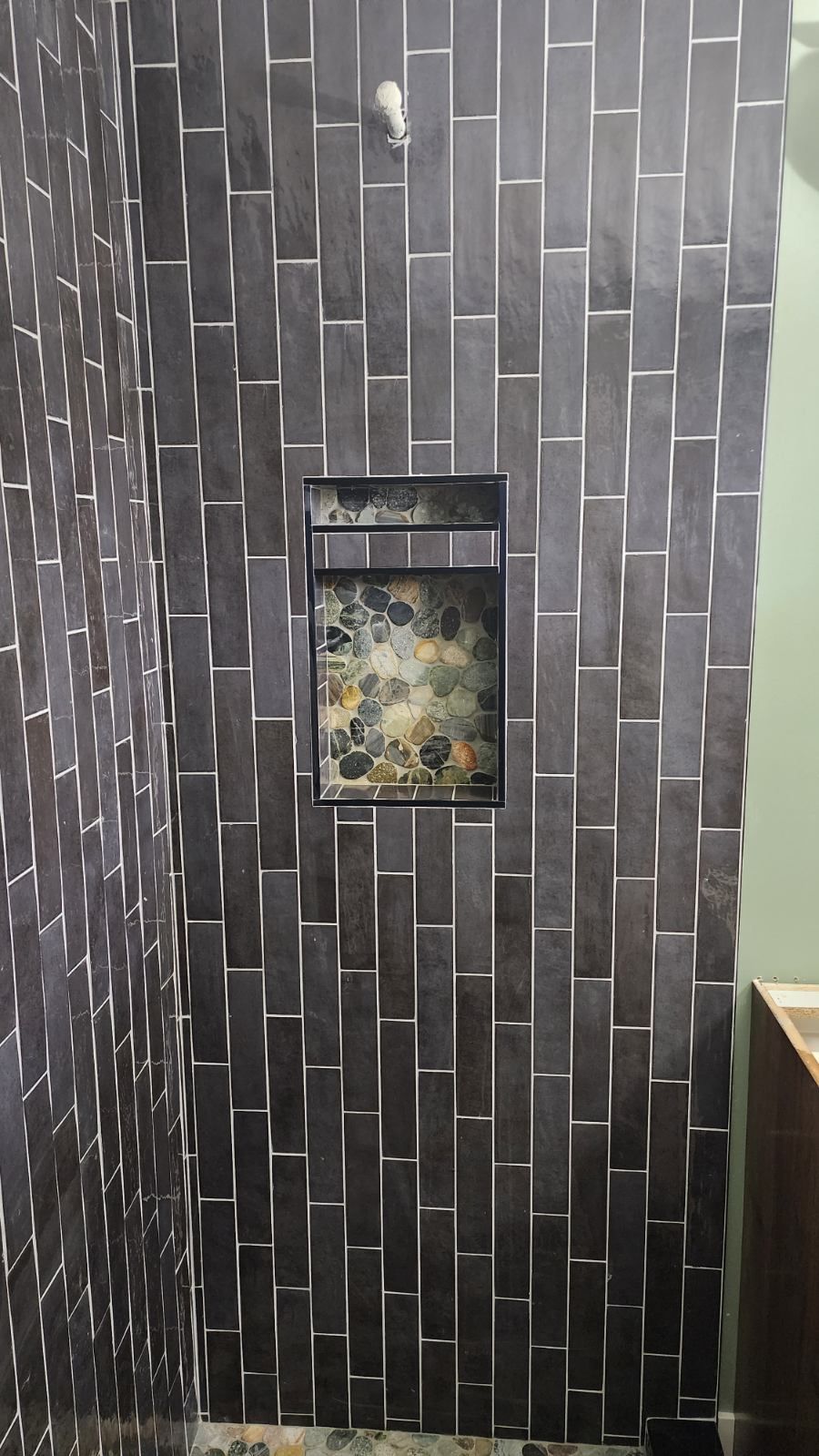 Dark tiled shower with built-in niche. Vertical, rectangular tiles with light grout.