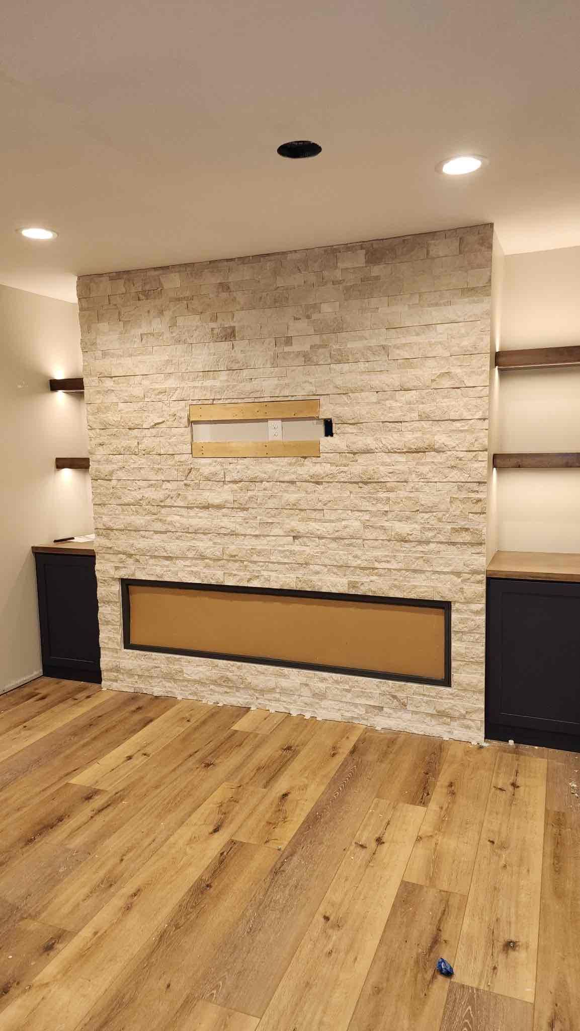 Fireplace with stone accent wall, wooden shelves, built-in cabinets, and hardwood floors.