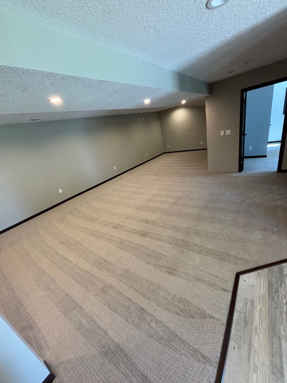 Empty room with light-colored carpet, grey walls, recessed lighting, and a dark doorway.