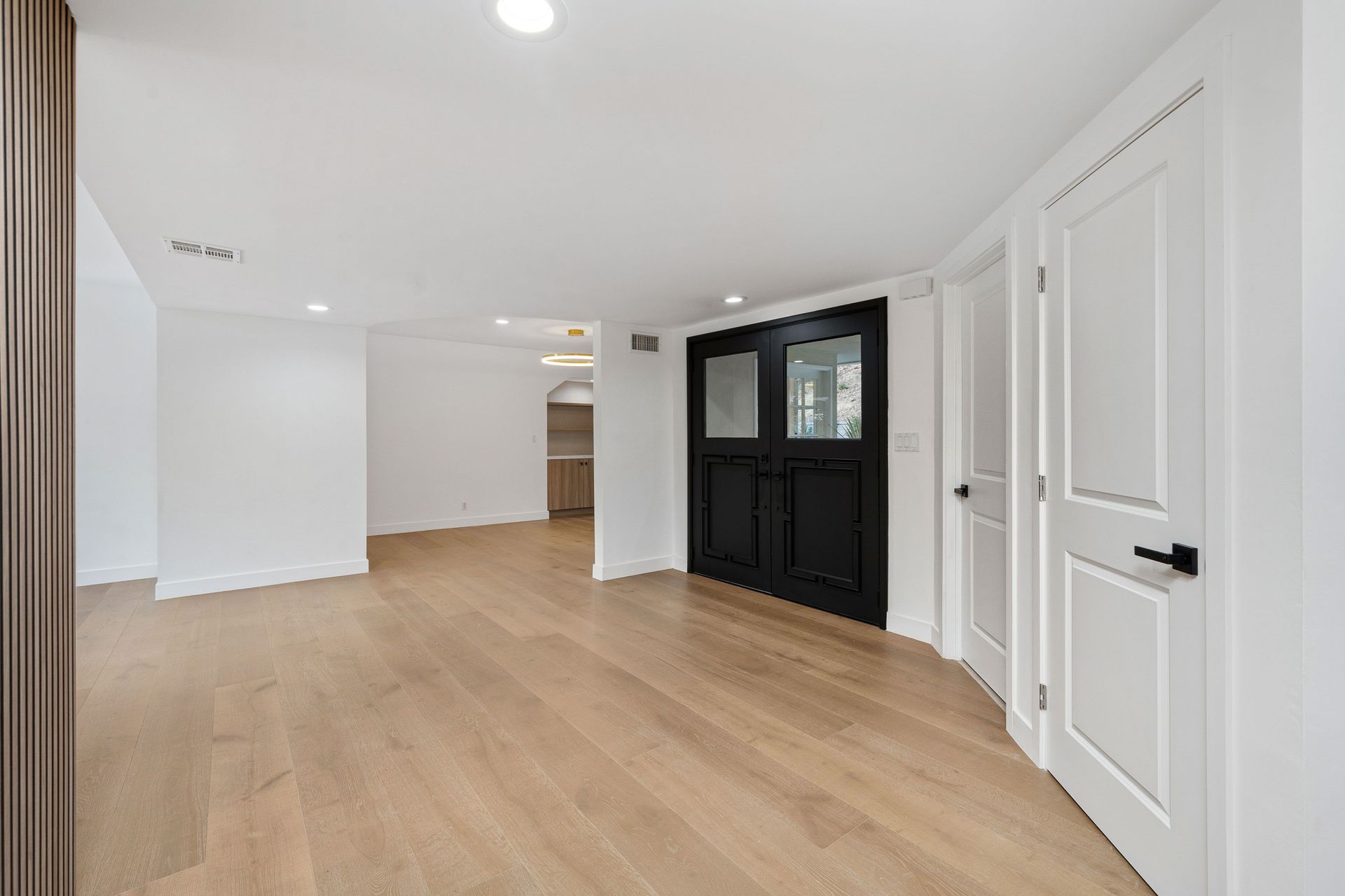 Empty room with wood floors, white walls, black double doors, and white doors.