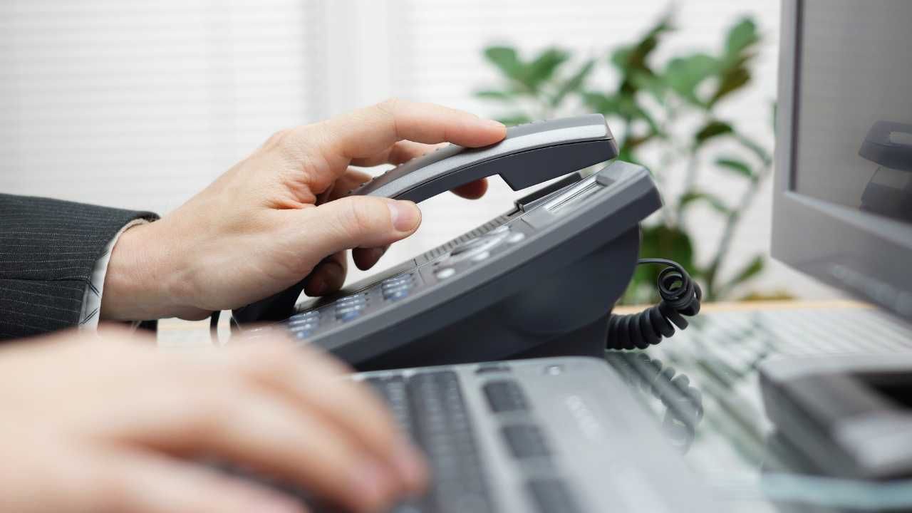 A person is using a telephone while typing on a keyboard.