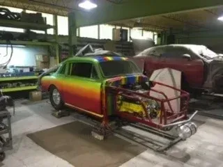 Rainbow-painted car shell in a workshop, mounted on a chassis with exposed frame and engine.
