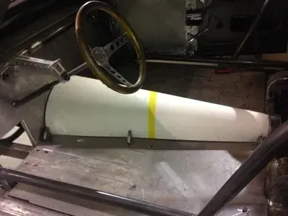 White cylindrical tank strapped with a yellow band inside a vehicle interior, near a steering wheel