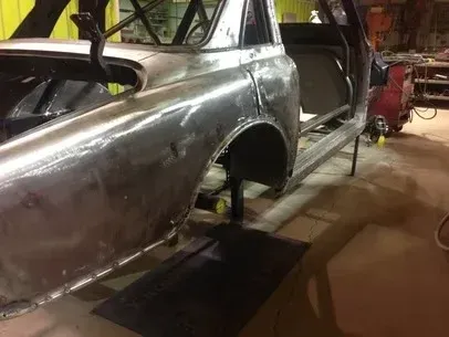 Partially restored silver car body in an auto shop, raised on stands with doors open