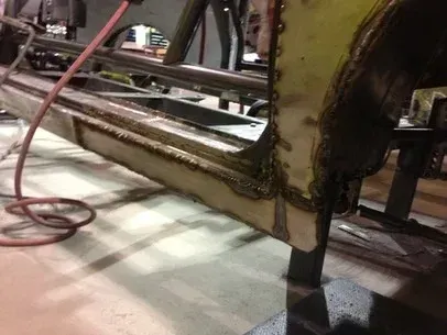 Rusty metal frame with a black support leg and red cables in an industrial setting