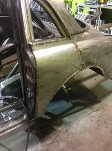 Rusty vintage car body shell in a workshop, shown from the side with exposed metal and no doors or windows