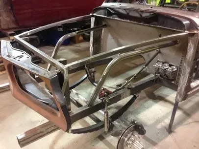 Metal car chassis frame on a workbench, showing exposed tubular structure and suspension components.