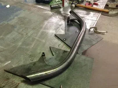 Curved metal motorcycle exhaust pipes on a workshop floor with tools and materials nearby