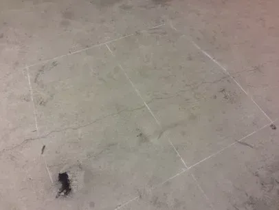 Scuffed beige floor with faint white tape markings and a small dark stain in the lower left corner