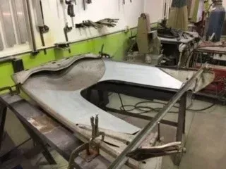 Workshop table with a large white car body panel being clamped in place on a metal frame