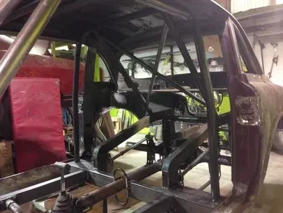 Roll cage inside a stripped race car chassis with exposed metal frame and red seat base