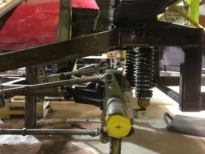 Close-up of a vehicle suspension and steering linkage with a yellow end cap in a garage.