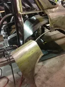 Close-up of a car body undergoing repair, with exposed metal panels and welding equipment.