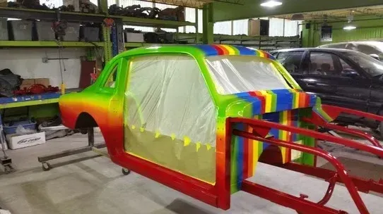 Rainbow-painted car body in a workshop, masked for painting with a red frame in front