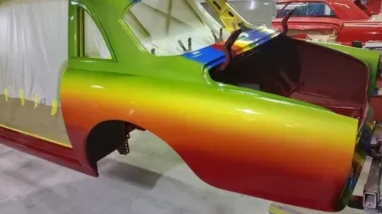 Partially assembled car body with a rainbow-gradient paint finish in a workshop