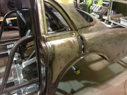 Rusty vintage car body shell in a garage, partially disassembled and mounted on a frame