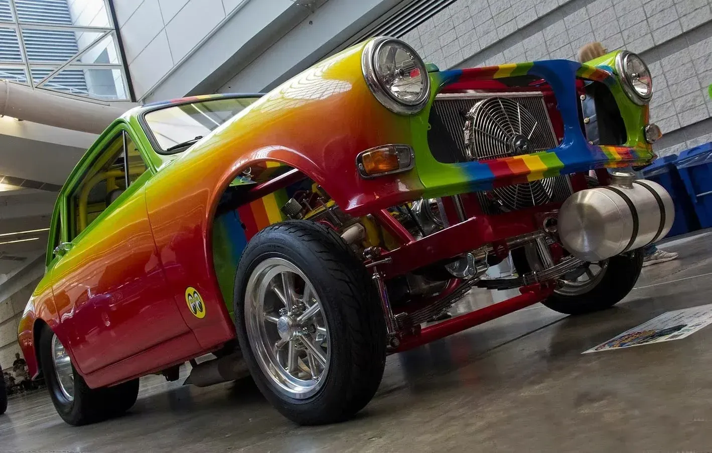 Rainbow-painted muscle car with chrome wheels and twin front exhausts, shot low in a garage