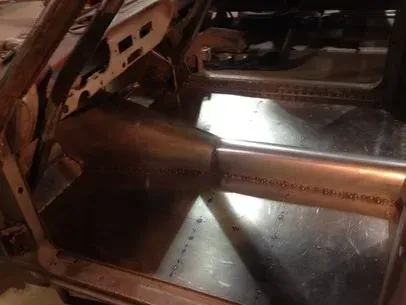 Interior of a rusty vehicle frame with a metal crossbar and reflective floor panel