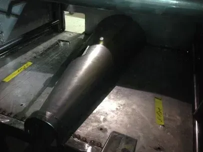 Large metallic cone-shaped object lying on a dark industrial floor inside a machine or compartment