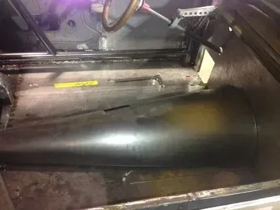 Large black cylindrical tank inside a dim industrial machine compartment, viewed from above.