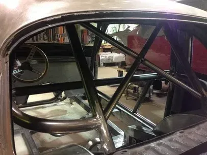 Interior of a car shell with black roll cage tubing and curved silver body frame in a workshop