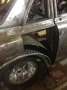 Damaged silver car with crumpled body panel and exposed rear wheel in a muddy setting