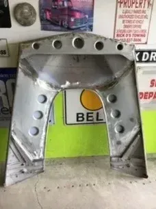 Large silver metal arch with circular holes, displayed indoors against a green wall with signs in the background