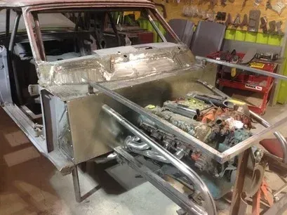 Custom car body under construction in a workshop, with exposed engine and unfinished metal panels.