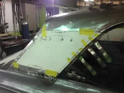 Car roof panel with taped-on white template in an auto body shop, showing marked cut lines and supports