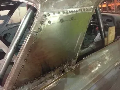 Metal race car interior with riveted panels and roll cage in a workshop