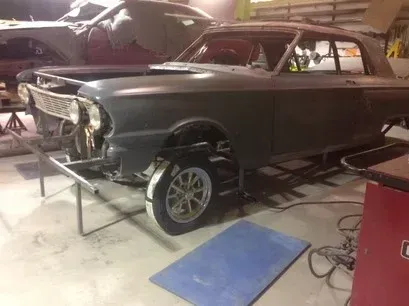 Partially restored classic car in a workshop, with missing front bumper and exposed front wheel.