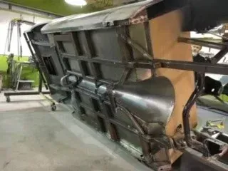 Large mechanical structure tipped on its side in a workshop, with metal frame and green components visible.