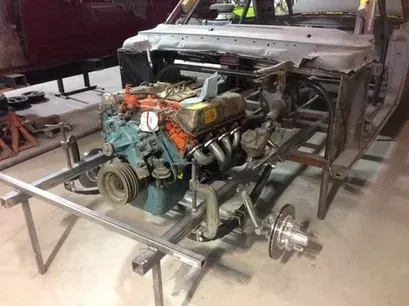 Bare car chassis with exposed V8 engine and front suspension in a garage
