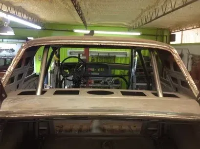 Damaged car body in a garage, with a stripped interior and missing windshield.