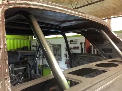 Rusty car body in a garage with exposed roll cage and interior framework