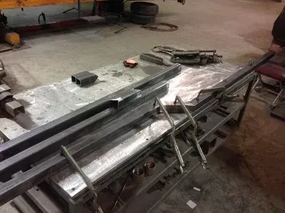 Metal beams and pipes stacked on a workbench in a workshop with tools and equipment nearby