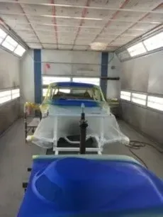 Cars in a spray booth, one covered with masking plastic and another blue-coated panel in front.