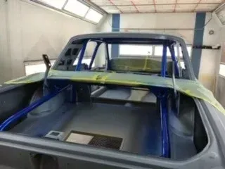 Blue pickup truck cab inside a repair booth, masked with tape and plastic for painting