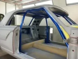 Car interior with blue roll cage and gray seats, shown in a workshop