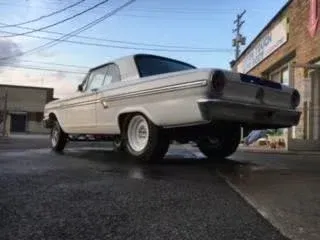 Low-angle view of a white classic muscle car parked on a city street near buildings