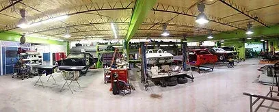 Wide indoor garage with several classic cars and work tables under bright ceiling lights
