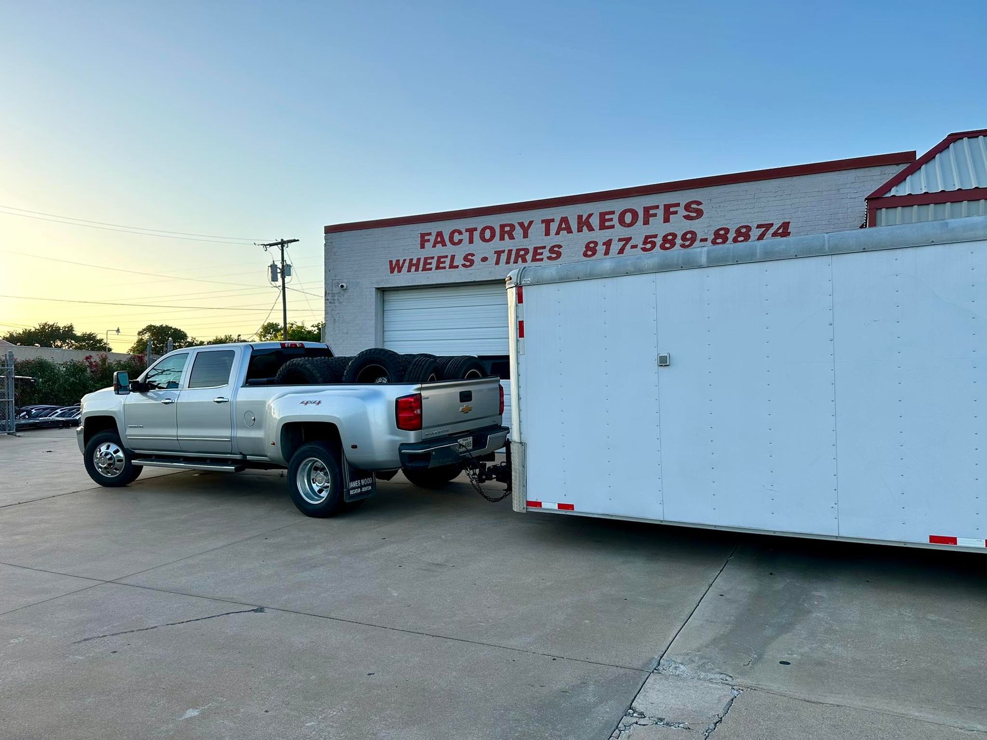A truck is pulling a trailer in front of a factory takeoffs building.