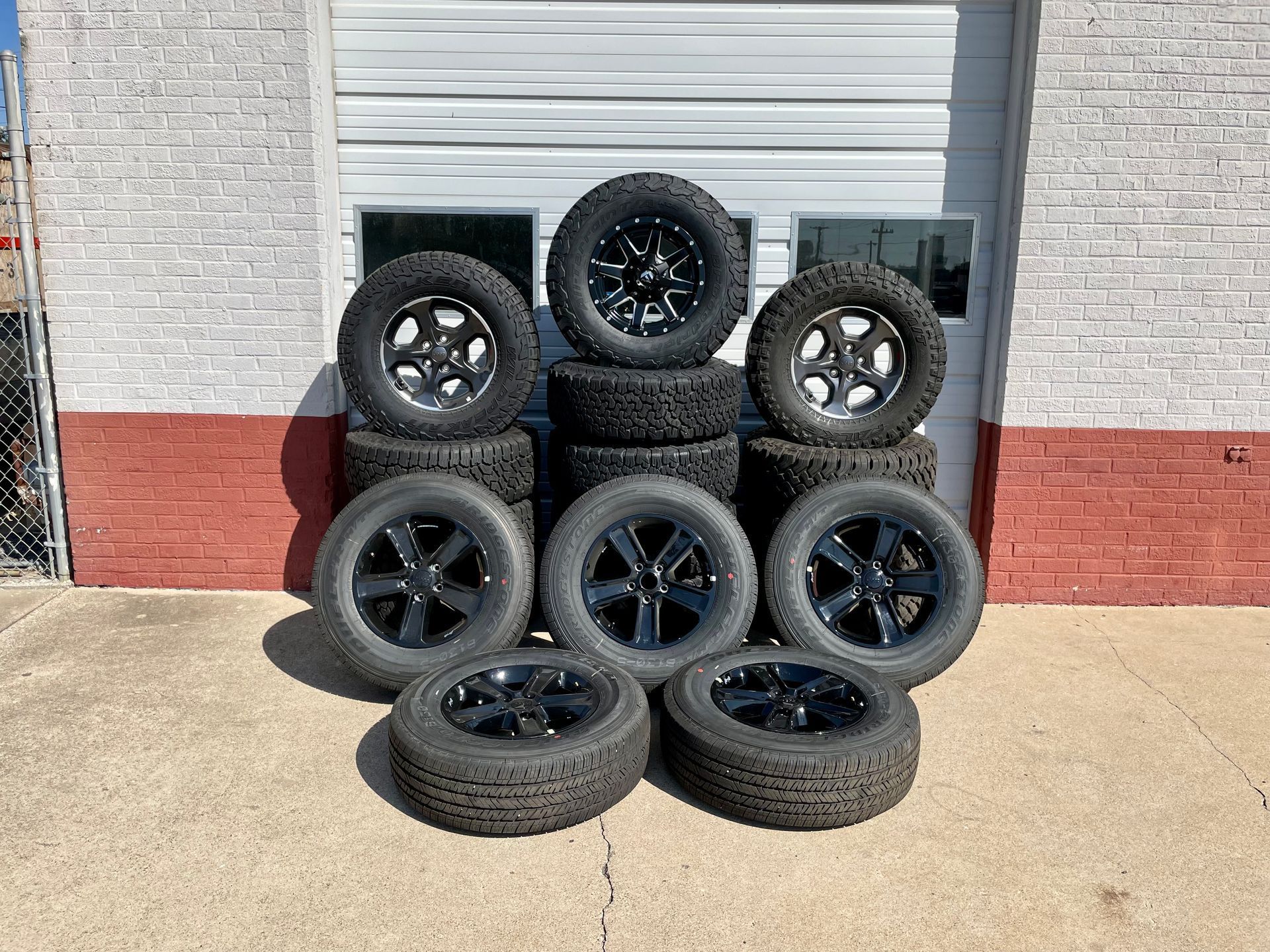 A bunch of tires and wheels are stacked on top of each other in front of a garage door.