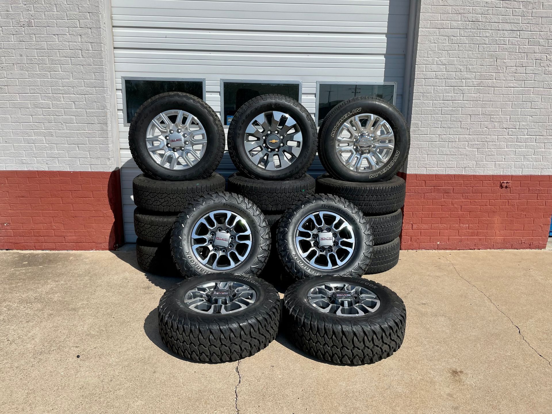 A bunch of tires and wheels are stacked on top of each other in front of a brick building.