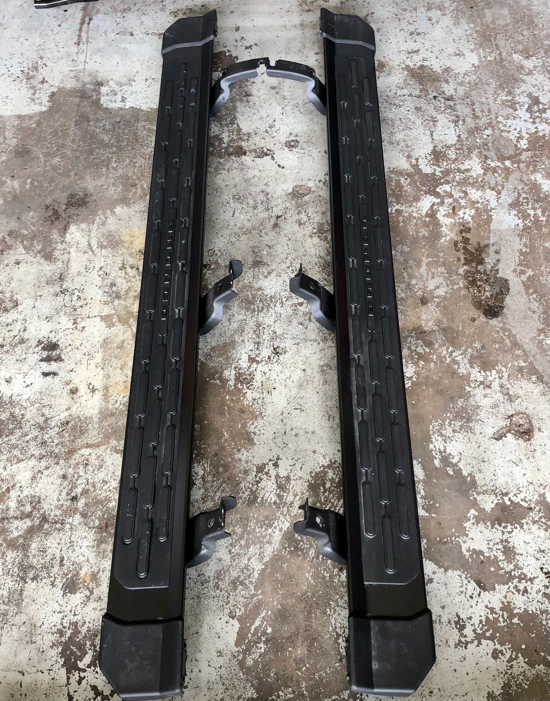 A pair of black side steps are sitting on a concrete surface.