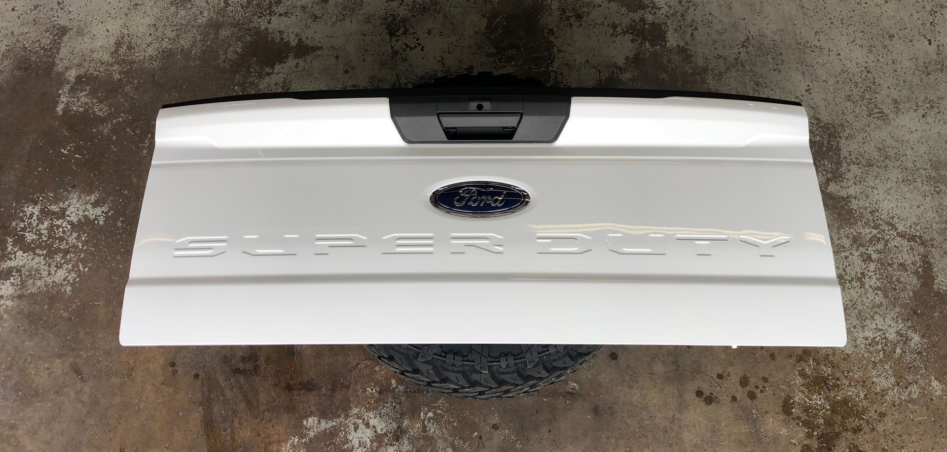 A white ford super duty tailgate is sitting on a concrete surface.
