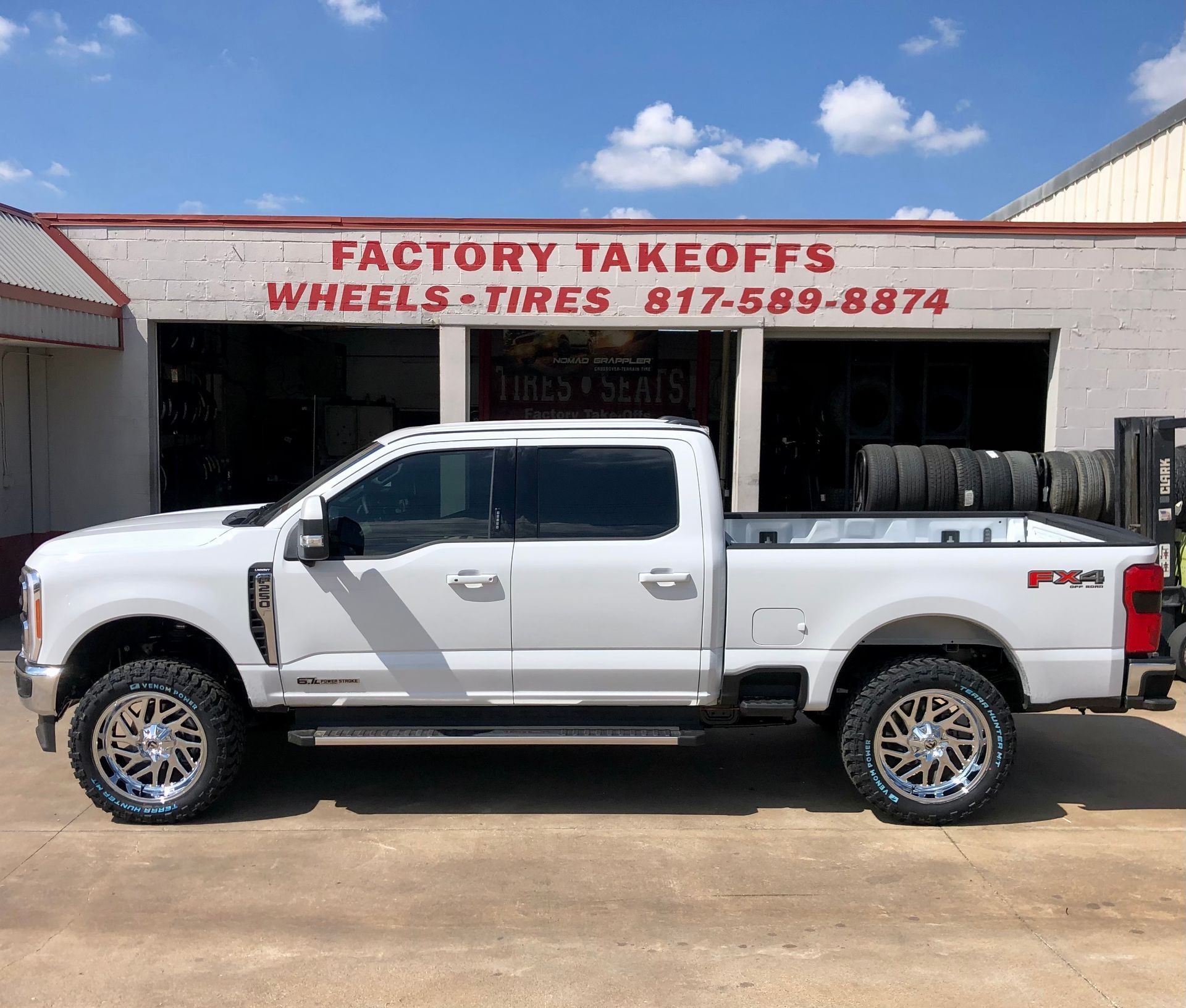 A white truck is parked in front of a factory takeoffs wheels and tires store.