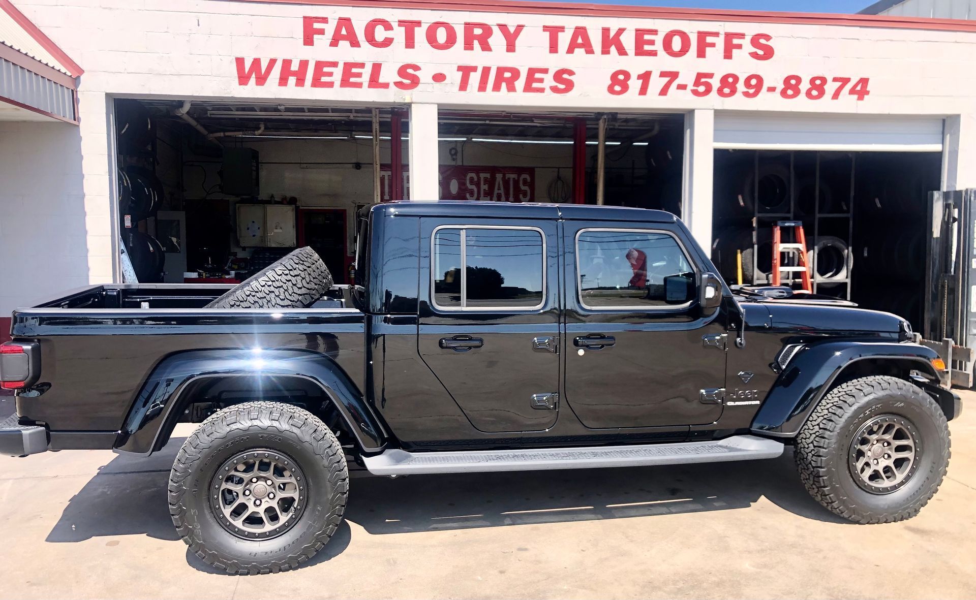A black truck is parked in front of factory takeoffs wheels tires
