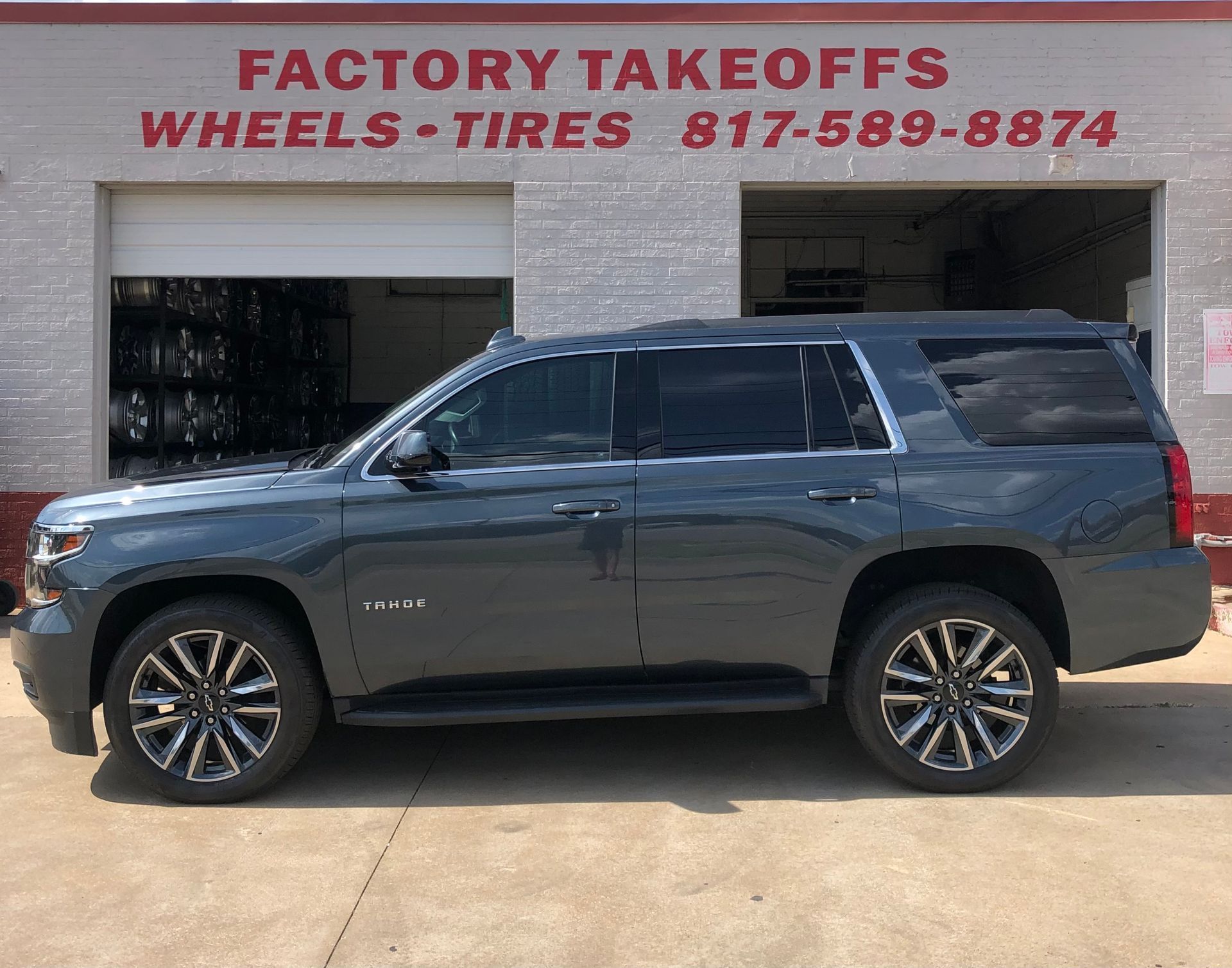 A gray suv is parked in front of a factory takeoffs wheels and tires store.