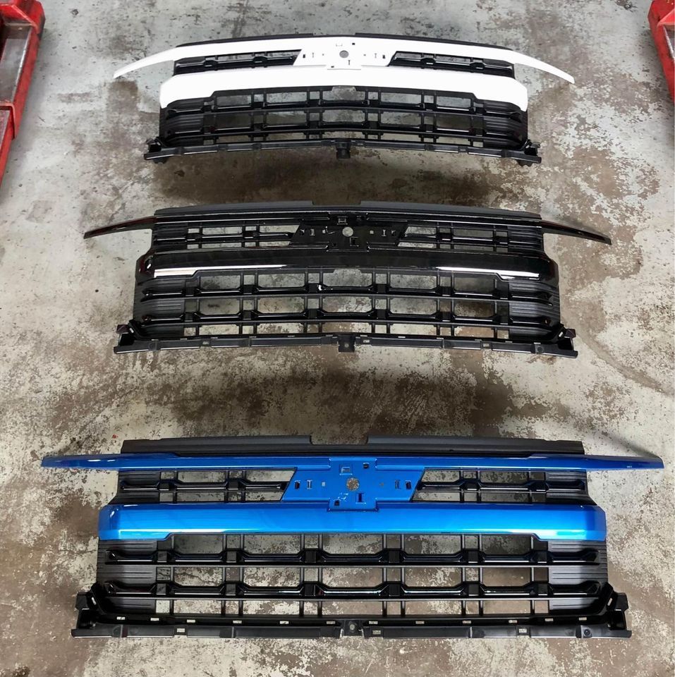 A row of different colored grilles are lined up on the ground